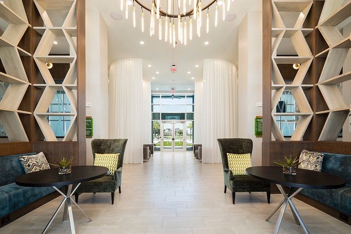 Elegant lobby with modern design, featuring geometric wood shelving, plush seating, and a striking chandelier.