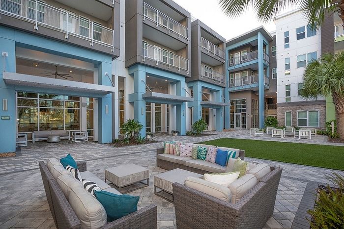 Modern apartment complex courtyard featuring stylish outdoor seating, lush greenery, and elegant architecture with spacious balconies.