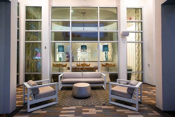 Elegant patio setting with modern white furniture, showcasing a cozy seating area against a backdrop of large glass windows revealing a stylish dining room inside.