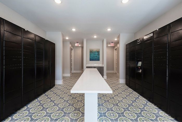 Modern mailroom with sleek black lockers, stylish patterned flooring, and ambient lighting for a sophisticated apartment experience.