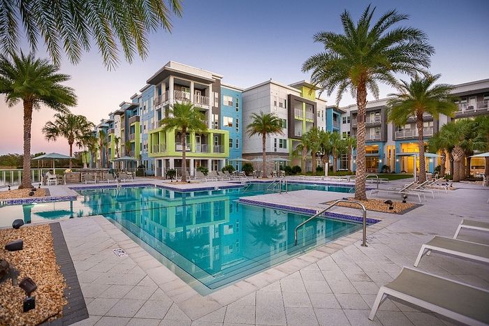 Luxurious apartment complex with vibrant modern design, featuring a stunning pool area surrounded by lush palm trees and contemporary architecture.