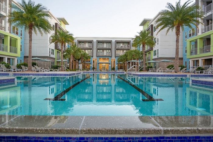 Luxurious apartment complex featuring a stunning pool area surrounded by palm trees and modern architecture, offering a tropical oasis for residents.