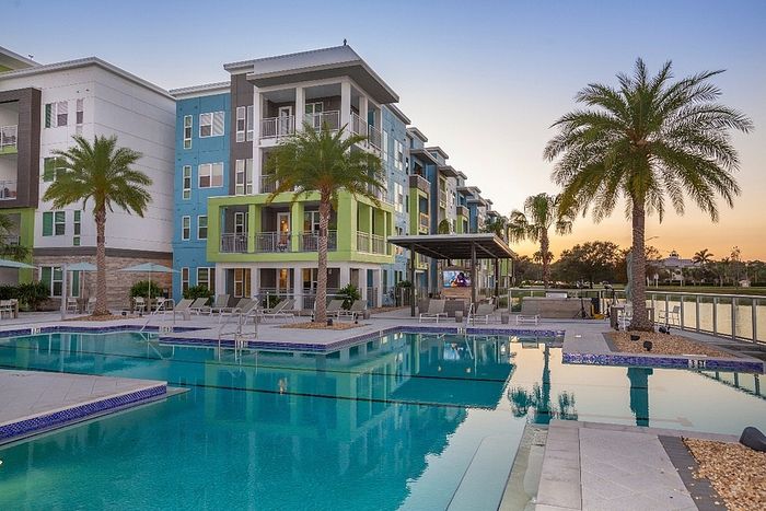 Modern apartment complex with vibrant colors, palm trees, and inviting pool area at sunset.