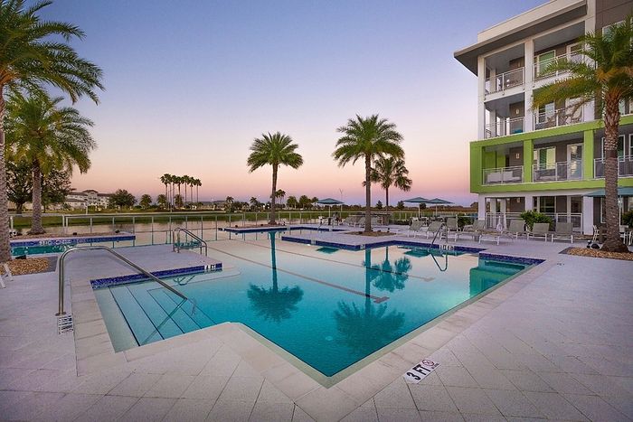 Luxurious apartment complex featuring a pristine outdoor pool surrounded by palm trees, perfect for leisure and relaxation.