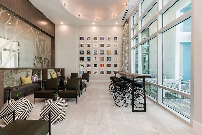 Modern communal area with elegant seating, geometric tables, and expansive windows, featuring contemporary art on the walls and bar seating.
