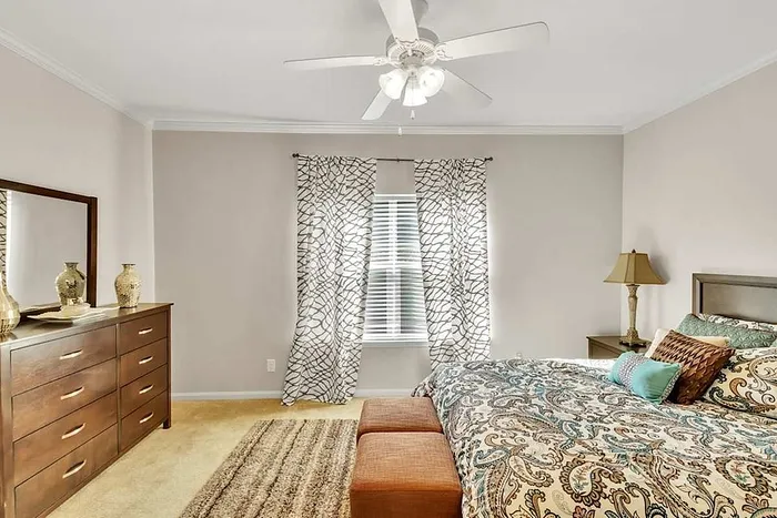 Elegant bedroom with stylish decor, featuring a wooden dresser, patterned curtains, and a cozy bed with vibrant bedding.