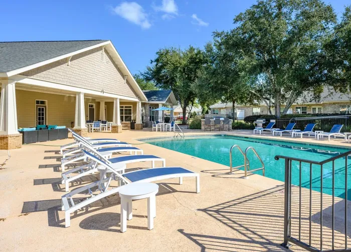 Luxurious outdoor pool area with elegant lounge chairs and shaded seating, surrounded by lush greenery and a stylish clubhouse, perfect for relaxation.