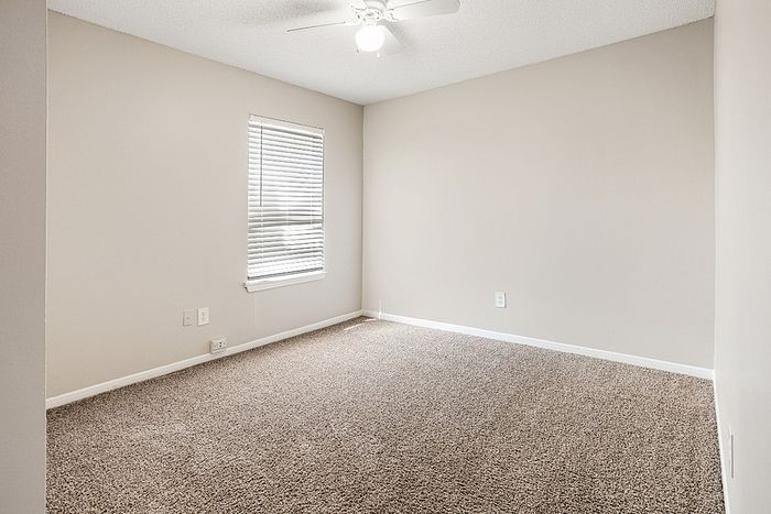 Bright and cozy carpeted bedroom with a ceiling fan and ample natural light from a window with blinds.