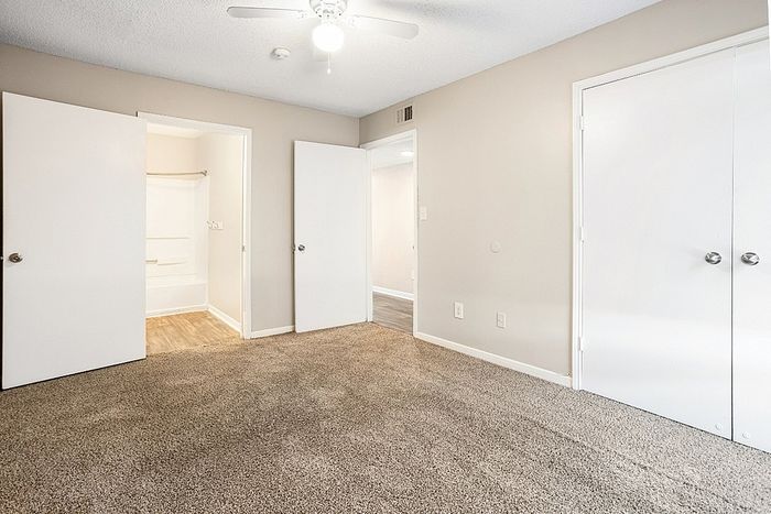 Bright and spacious carpeted bedroom with neutral walls, ceiling fan, and ample closet space, perfect for a cozy retreat.