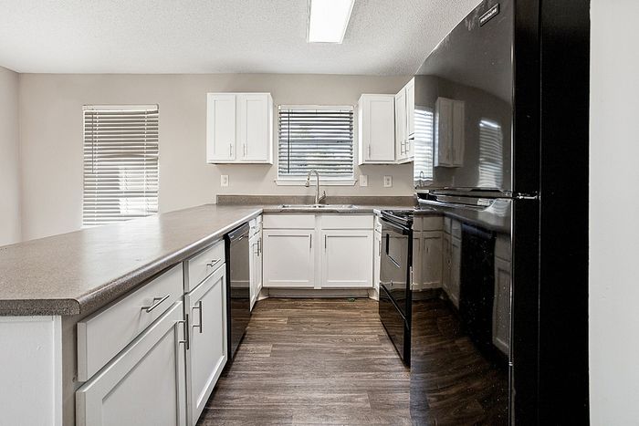 Elegant kitchen with modern black appliances, sleek dark countertops, and bright white cabinetry complemented by natural light and stylish blinds.