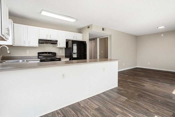 Bright open-plan kitchen and living area with modern white cabinets, sleek countertops, and stylish wood flooring.