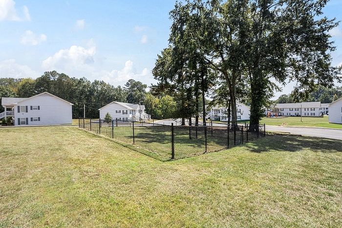 Charming residential complex with lush grassy areas, mature trees, and white buildings under a clear blue sky.
