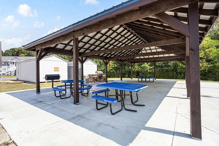 Inviting outdoor pavilion with blue picnic tables and grill area, perfect for gatherings and relaxation in a beautiful community setting.