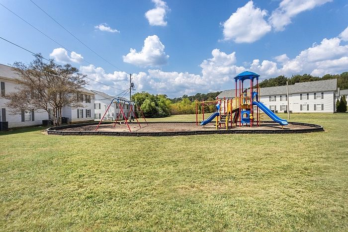 Inviting apartment complex with a vibrant playground, surrounded by lush greenery, perfect for families and outdoor enjoyment.