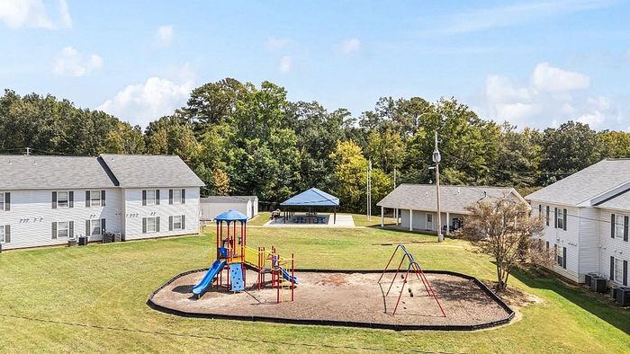 Inviting apartment complex with spacious outdoor area featuring a colorful playground, surrounded by lush greenery and well-maintained buildings.