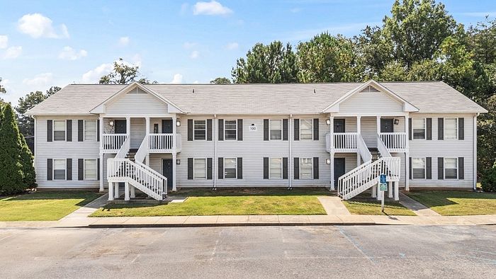 Charming two-story apartment building with white siding, featuring elegant staircases and lush green surroundings.