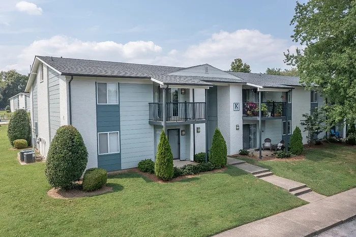 Charming apartment complex with modern balconies and lush green landscaping under a bright blue sky.