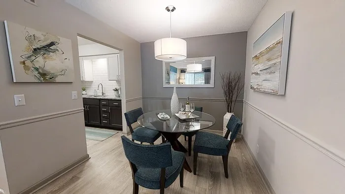 Chic dining room with a glass-top table, elegant lighting, and modern artwork, adjacent to a stylish kitchen.