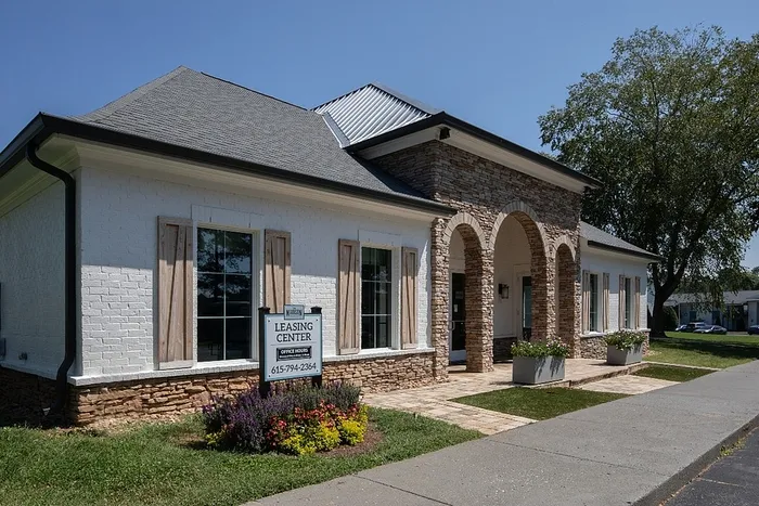 Charming leasing center with elegant stone archways, welcoming ambiance, and vibrant landscaping under a clear blue sky.