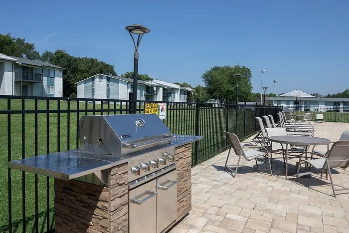 Chic outdoor patio area featuring a modern stainless steel grill, elegant seating, and lush green surroundings, perfect for entertaining.
