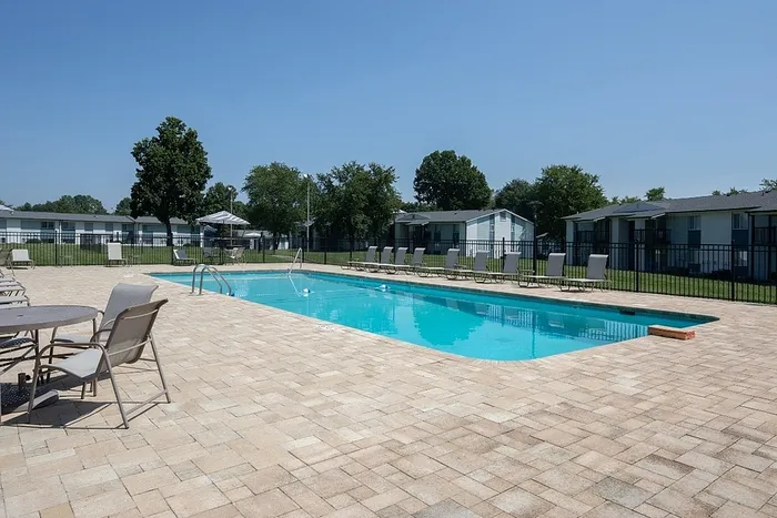 Refreshing outdoor swimming pool with relaxing sun loungers and patio seating, surrounded by lush greenery in a tranquil apartment community.