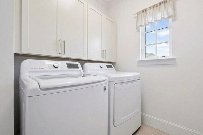Bright and efficient laundry room featuring modern appliances, sleek white cabinetry, and a charming window view.