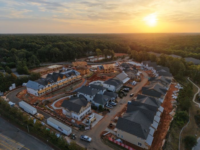 Aerial view of a vibrant residential development, showcasing newly constructed homes surrounded by lush greenery at sunset.