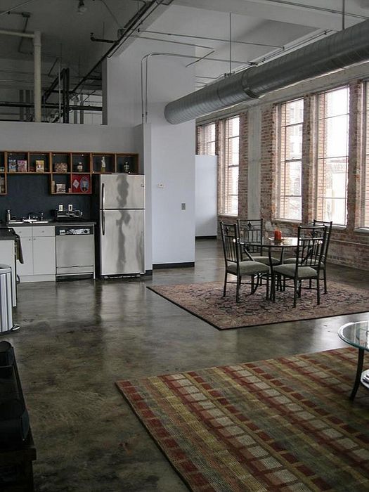 Chic urban loft with exposed brick, large windows, modern kitchen, and cozy dining area.
