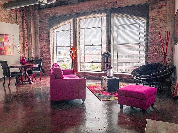 Chic urban loft with exposed brick walls, large industrial windows, and vibrant pink furnishings for a modern, stylish living space.