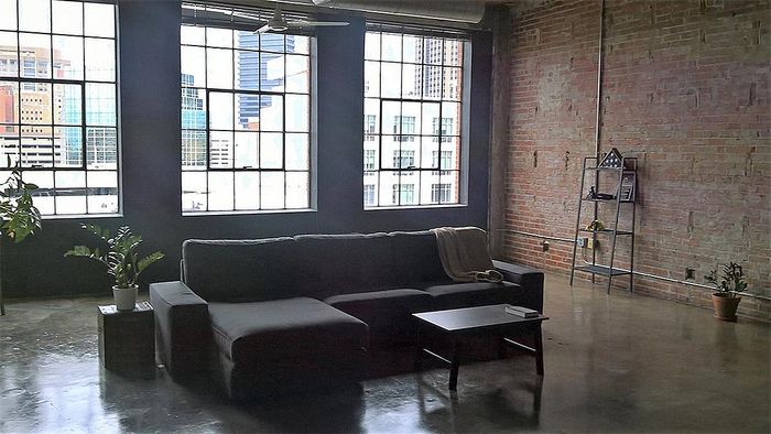 Chic urban loft with large industrial-style windows, exposed brick walls, and modern furnishings offering a cozy ambiance.