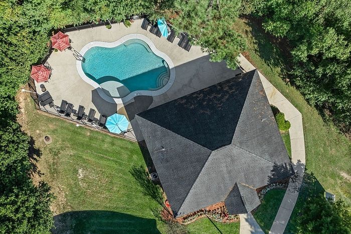 Aerial view of a pristine residential pool area with vibrant umbrellas, plenty of seating, lush green surroundings, and adjacent building.