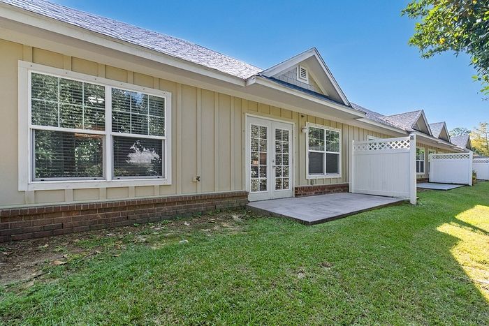 Charming single-story home exterior with modern French doors opening to a lush green backyard and spacious patio area.