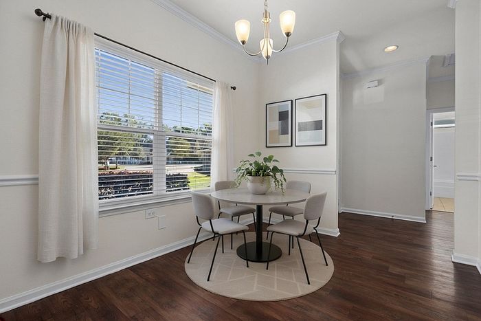 Bright dining nook with elegant chandelier, round table, and modern art, overlooking lush greenery through large window.