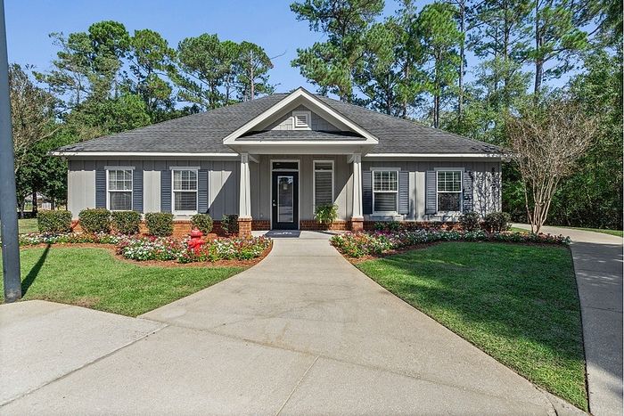 Charming single-story house with elegant gray facade, surrounded by lush greenery and colorful flower beds.
