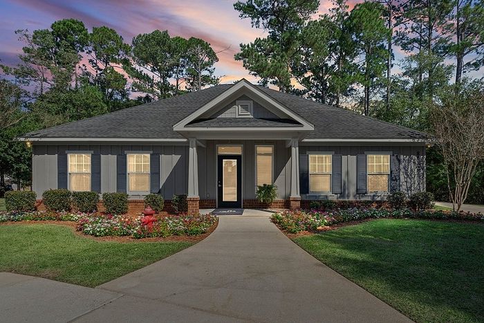 Charming gray home with beautiful landscaping and inviting walkway, set against a serene backdrop of tall trees at sunset.