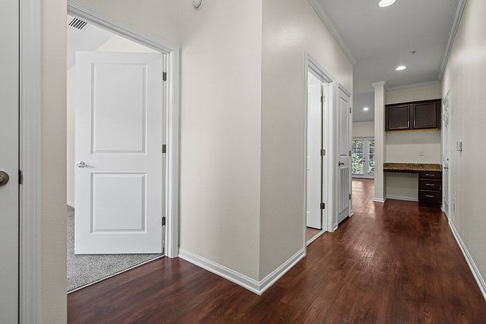 Inviting apartment hallway with warm wood flooring, modern cabinetry, and a glimpse into bright, spacious rooms.