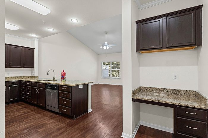 Modern open-concept apartment with a sleek kitchen featuring granite countertops, dark cabinetry, and elegant hardwood floors connecting to a bright living area.