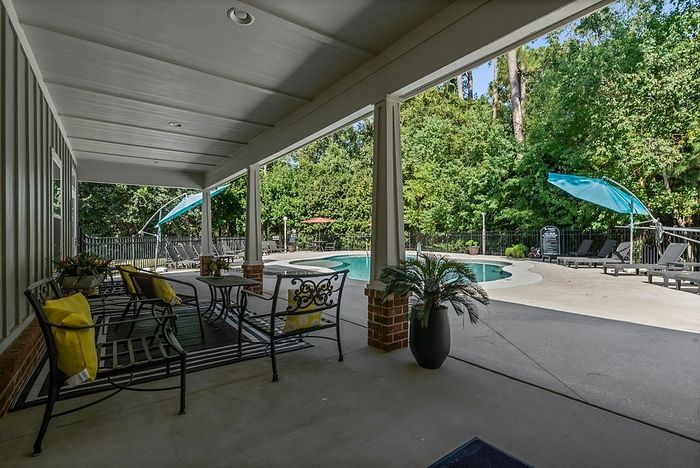 Inviting outdoor space featuring a covered patio with elegant seating overlooking a sparkling pool and lush greenery.
