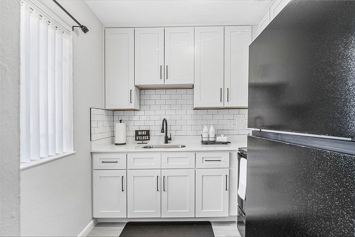 Contemporary kitchen with sleek black appliances, stylish white cabinets, and a modern subway tile backsplash.