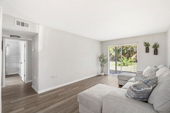 Bright, modern living room with sliding glass door leading to a lush garden, featuring a cozy sectional sofa and elegant decor accents.
