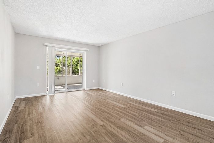 Bright, spacious living room with elegant wood flooring and large glass doors leading to a sunny patio.