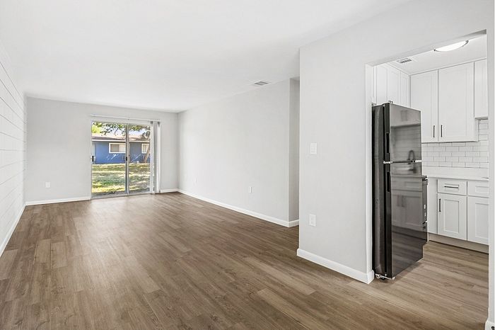 Bright and inviting apartment interior featuring an open living space with elegant wood flooring, large glass doors leading to a lush outdoor view, and a modern kitchen with sleek stainless steel appliances and white cabinetry.
