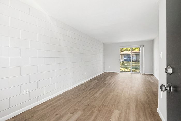 Bright and spacious living room with elegant wooden flooring and large glass doors opening to a scenic backyard view.