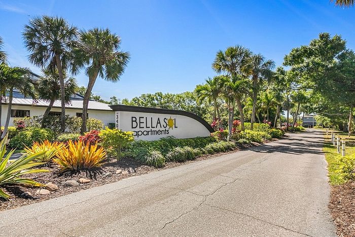 Welcoming entrance to Bella Sol Apartments surrounded by lush tropical landscaping and vibrant greenery under a clear blue sky.