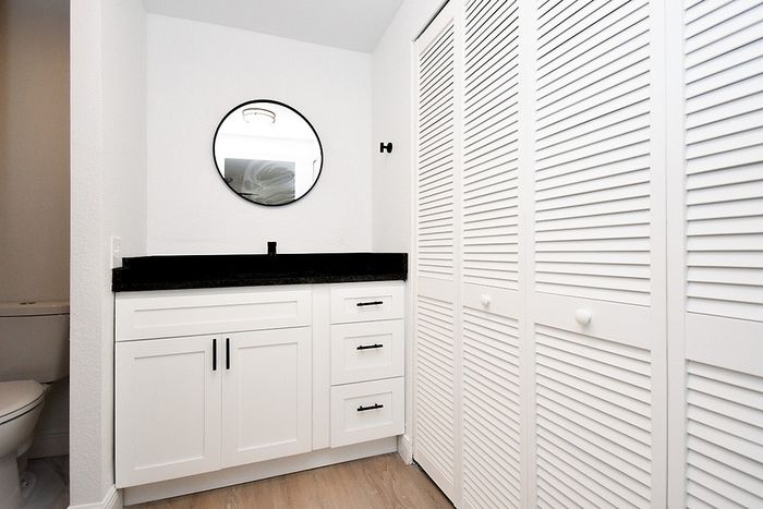 Chic bathroom design with sleek white cabinetry, a round mirror, and modern black counter, accentuated by stylish louvered doors.