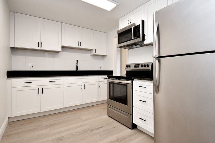 Modern kitchen with sleek stainless steel appliances, white cabinetry, and elegant black countertops in a stylish apartment.