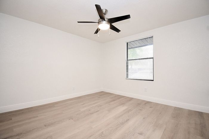 Bright and airy bedroom with sleek wooden flooring, modern ceiling fan, and large window for natural light.