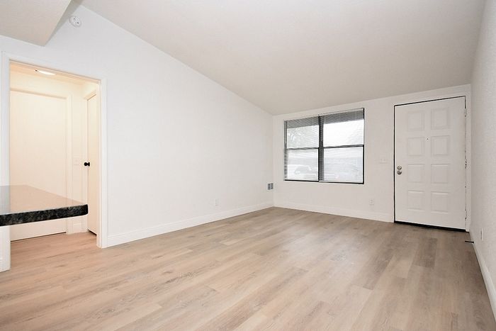 Bright and spacious living area with elegant hardwood flooring, a large window providing natural light, and a sleek entryway.