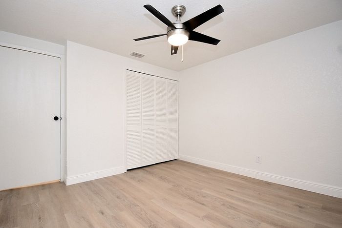 Bright, freshly painted room with sleek wood flooring, modern ceiling fan, and ample closet space in stylish apartment.
