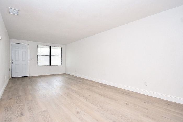 Bright and airy apartment with sleek hardwood floors, white walls, and ample natural light from a large window.